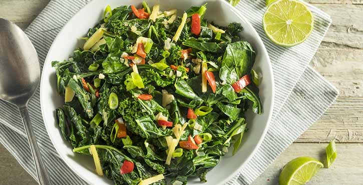 An overhead photo of a white bowl full of steamed green leaves and vegetables.