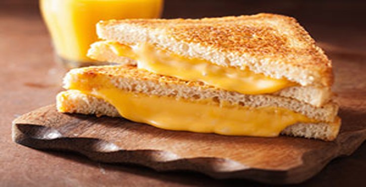 A delicious grilled cheese sandwich, golden brown and melted, served on a wooden cutting board with a glass of orange juice in the background.