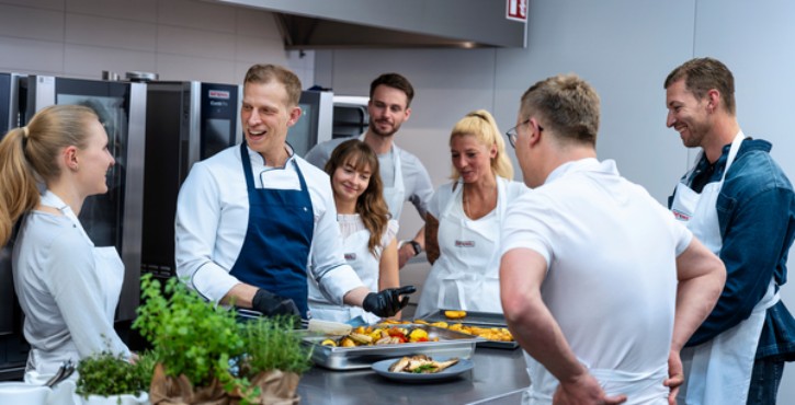 Chef presenting roasted vegetables to group in front of RATIONAL iCombi Pro combi-steamer.