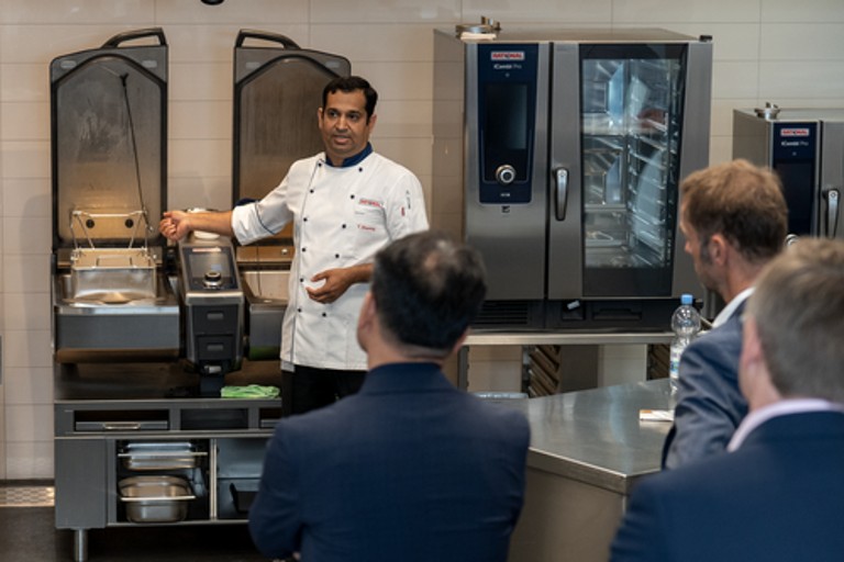 Chef presenting RATIONAL iVario Pro and iCombi Pro cooking systems to group in training kitchen.