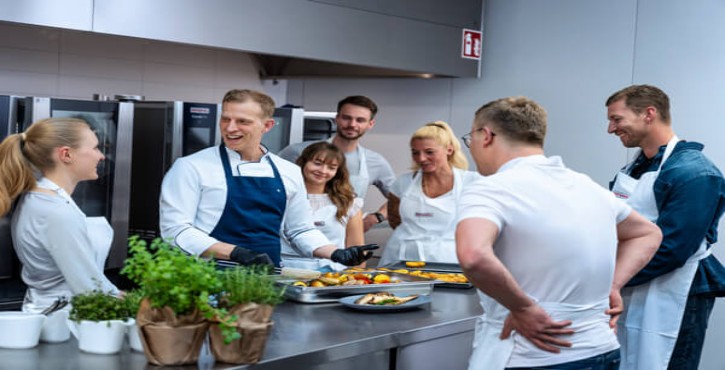 Chef presenting roasted vegetables to group in front of RATIONAL iCombi Pro combi-steamer.