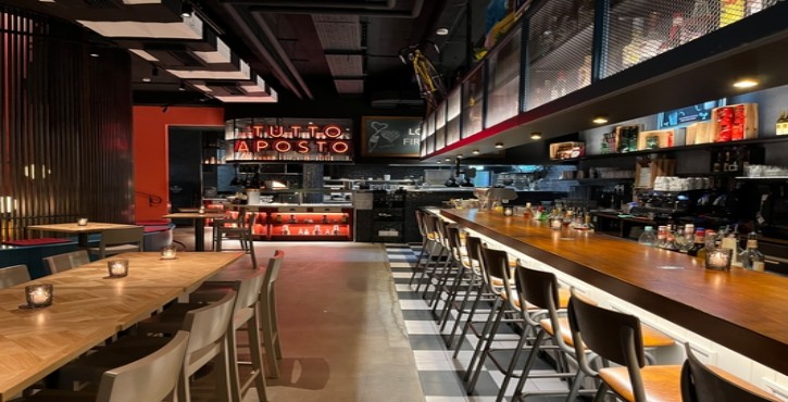 Modernes Restaurant mit langer Bar, Holztischen, stimmungsvoller Beleuchtung und offener Küche.