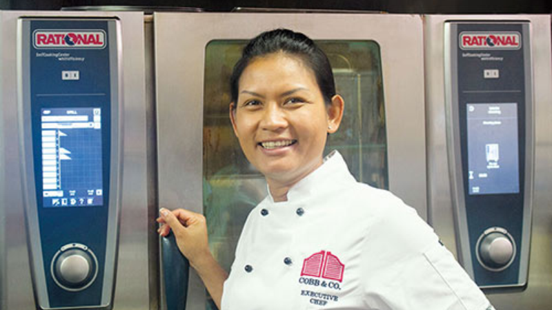 A chef wearing a uniform with the "Cobb & Co" logo is standing in front of two Rational SelfCookingCenter ovens, smiling at the camera.