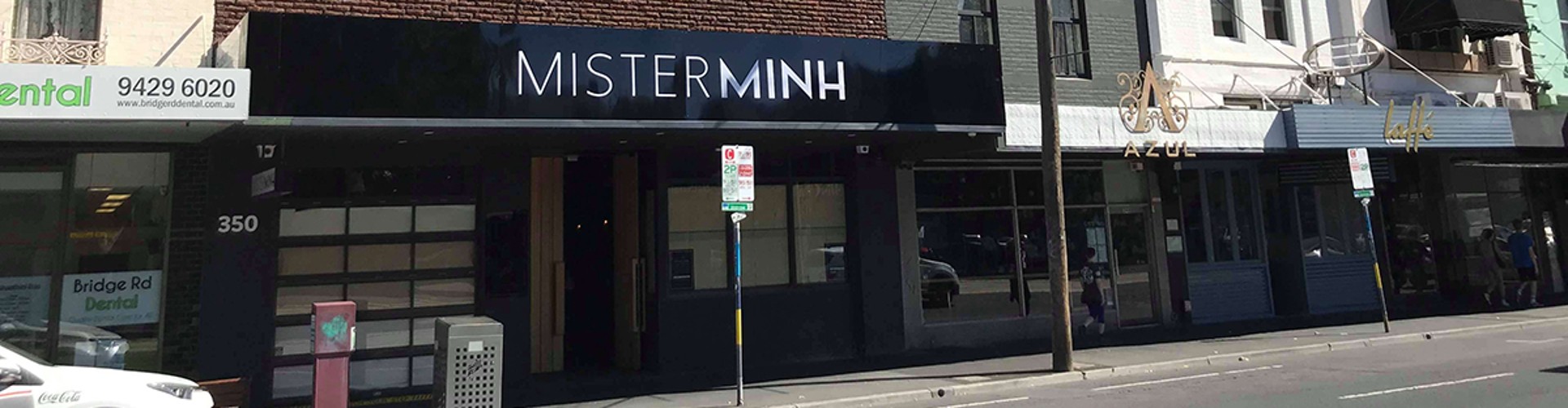 A street view of the "MISTER MINH" restaurant with other shops and clear blue sky.