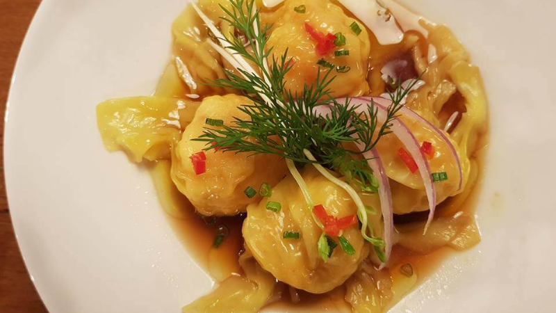 A plate of dumplings with sauce, garnished with red peppers, onions, and herbs.