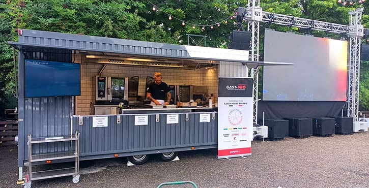 Venkovní gastro kontejner s RATIONAL iCombi Pro a iVario Pro vedle eventové obrazovky.