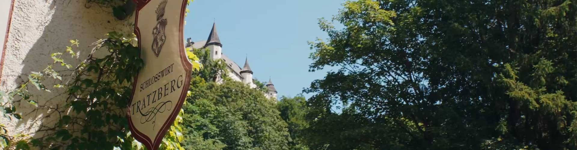 Schild des Schlosswirt Tratzberg mit Burgtürmen über den Bäumen.