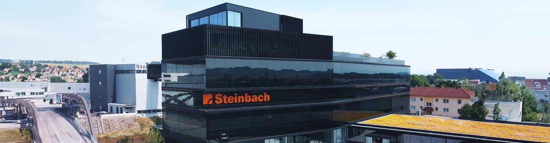Luftaufnahme des Bürogebäudes von Steinbach mit dunkler Glasfassade und Gründach.