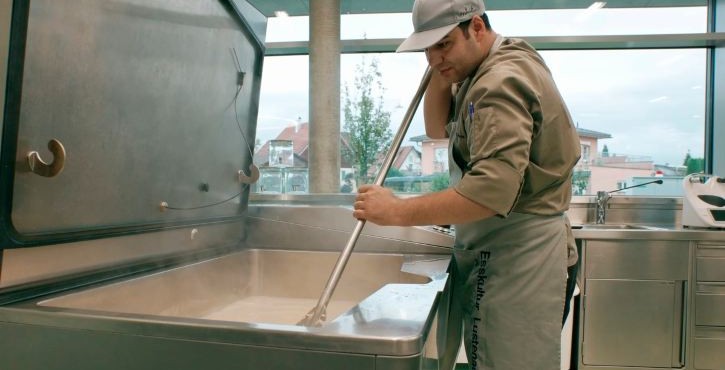 Koch rührt Speisen in einem großen offenen Garkessel in einer Profiküche.