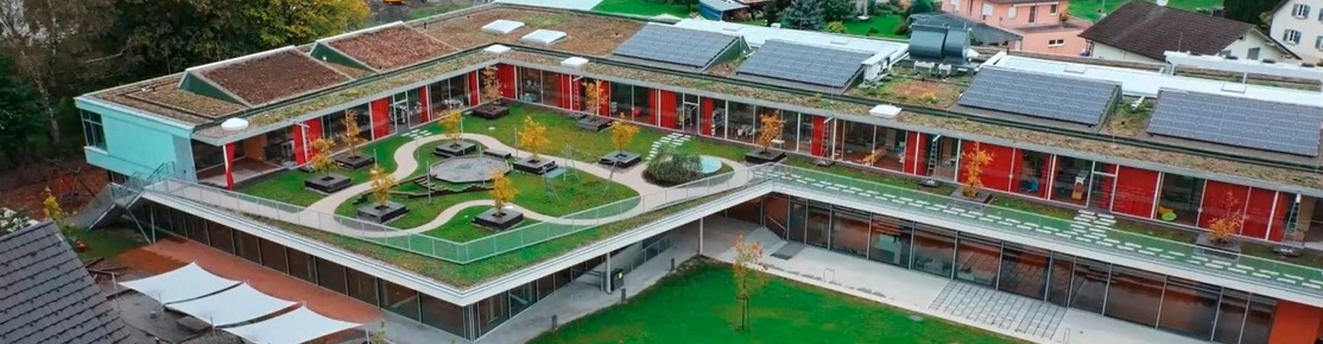 Luftaufnahme eines modernen Gebäudekomplexes mit Gründach, Solaranlagen und Innenhof.