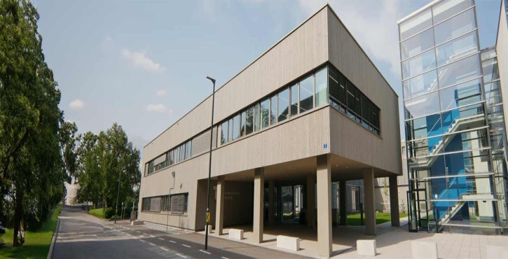 Moderne Architektur der Tourismusschule Klessheim mit verglastem Treppenhaus und Bäumen im Umfeld.