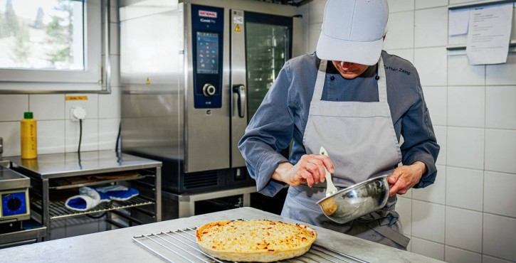 Köchin glasiert pikanten Kuchen neben RATIONAL iCombi Pro Kombidämpfer in Profiküche.