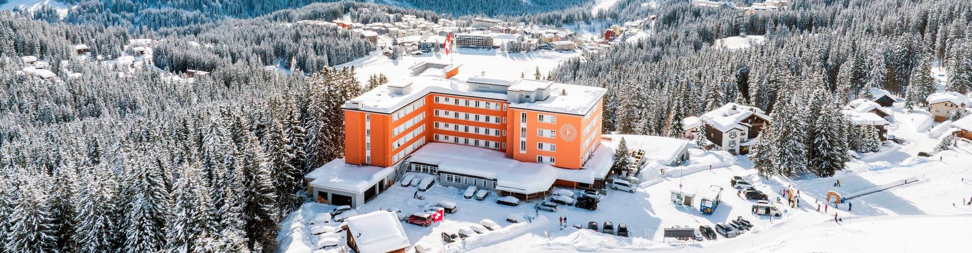 Luftaufnahme eines roten Gebäudes inmitten verschneiter Berge und Wälder in den Schweizer Alpen.