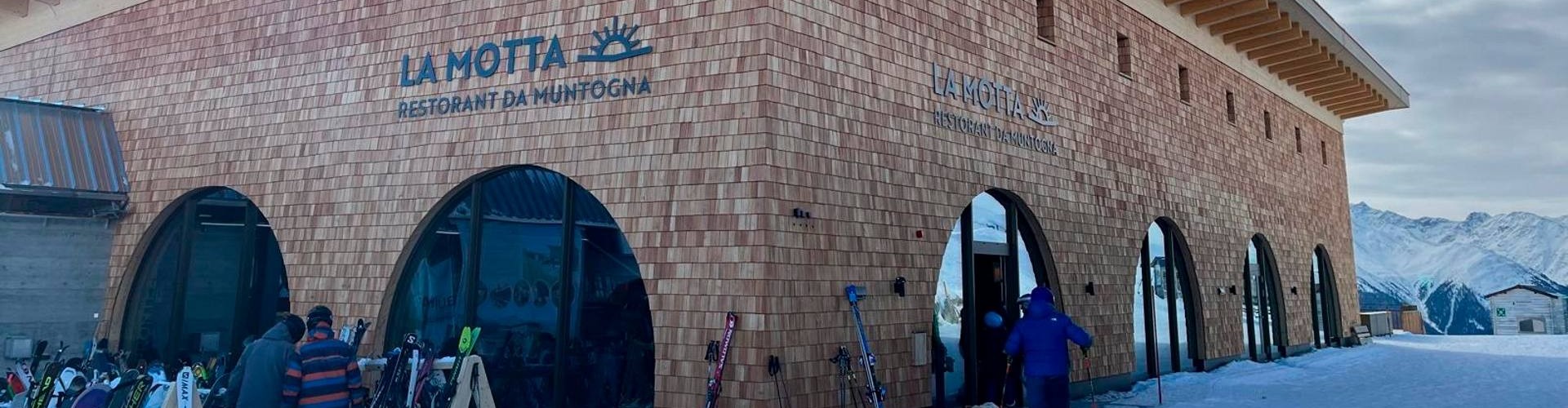 Skifahrer vor dem LA MOTTA – Restorant da Muntogna, einem alpinen Holzrestaurant in den Bergen.