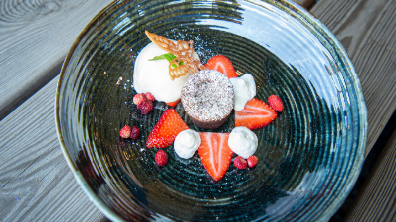 Gourmet-Dessert mit Schokoladenfondant, Schlagsahne, Eis, Erdbeeren und Waldbeeren, kunstvoll angerichtet.