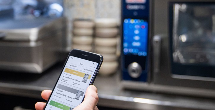 One person is holding a smartphone on which ConnectedCooking can be seen. In the background an iCombi Pro and an iVario XS.