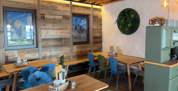 Gemütliche Sitzecke mit bunten Stühlen im Alpenstil, Holztischen und rustikaler Holzvertäfelung.