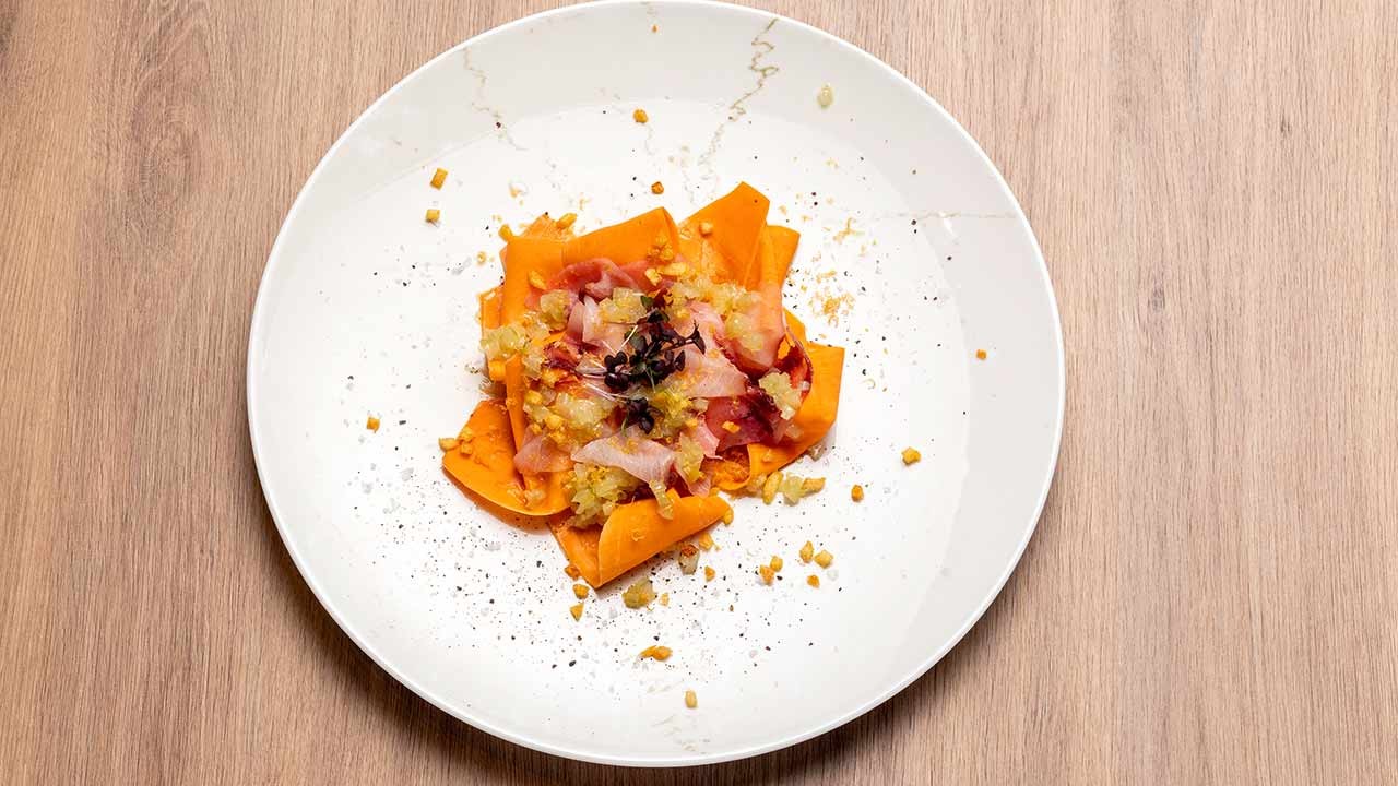 Moderner Restaurantteller mit dünn geschnittenem Gemüse und zartem Fisch, garniert mit Zitrus und Microgreens auf Holztisch.