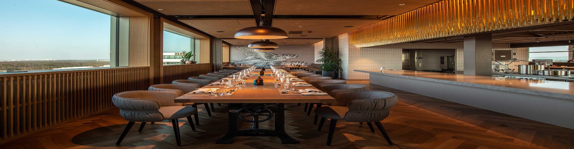 Eleganter Restaurantbereich mit langem gedecktem Tisch, offener Küche und großen Fenstern mit Stadtblick.