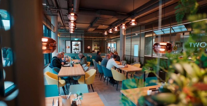Modern canteen with people dining at wooden tables in a brightly lit interior.