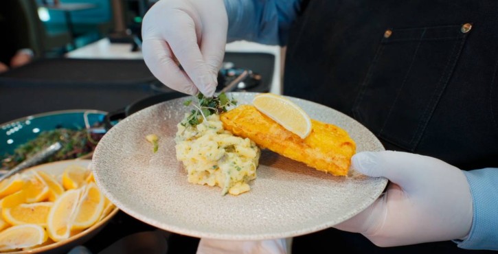 Chef plating mashed potatoes and breaded fish fillet with lemon and herbs.