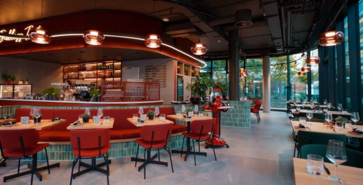 Modern restaurant interior with red and green seating, open bar and elegant lighting.