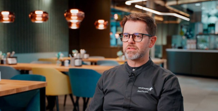 Chef in Aramark uniform giving interview in modern restaurant setting.