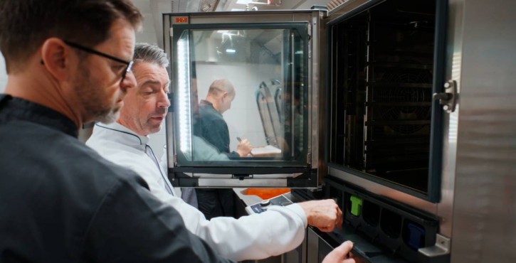Two chefs discussing settings of an open RATIONAL iCombi Pro combi oven in kitchen.