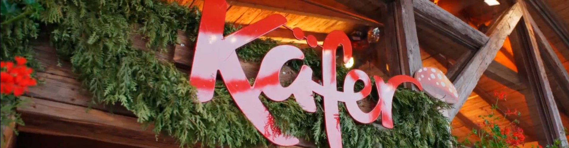 Eingang zum Käfer-Restaurant mit Tannenzweigen und roten Blumen dekoriert.