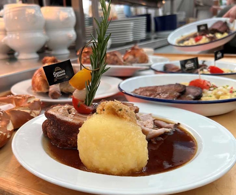 Braten mit Soße, Kartoffelknödel und Rosmarin auf angerichtetem Teller.