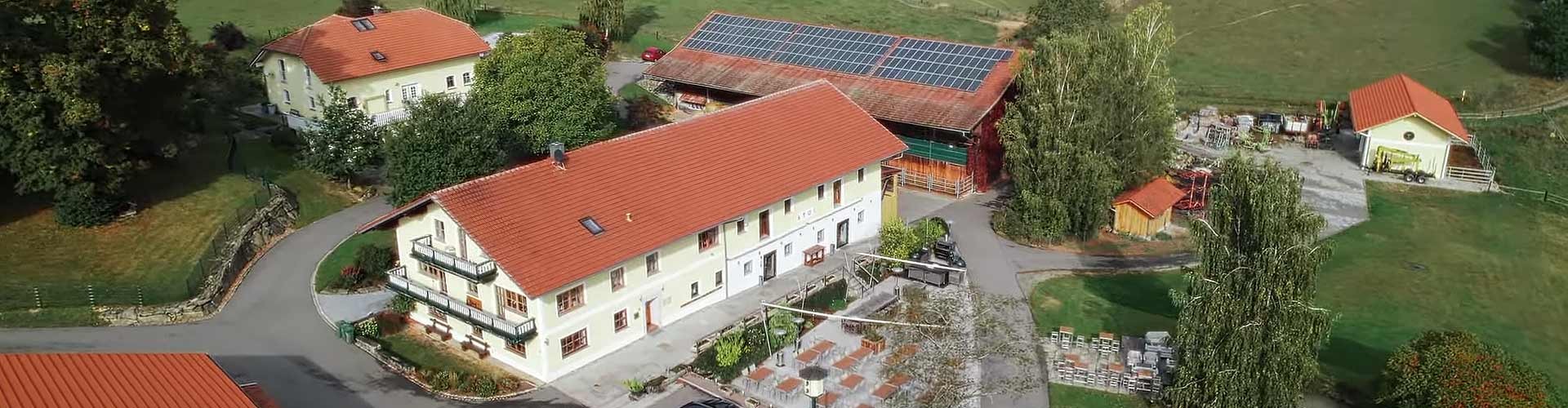 Luftaufnahme eines ländlichen Anwesens mit roten Dächern und Solaranlage im Grünen.