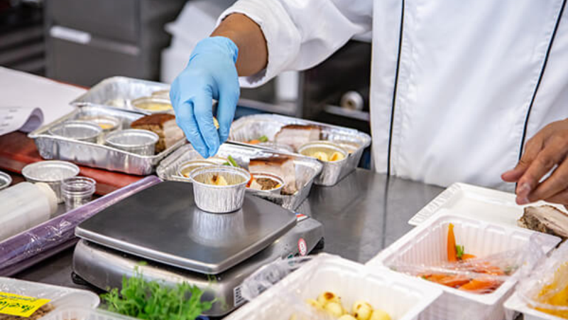 Chef arranging meal components in trays on a kitchen worktop.