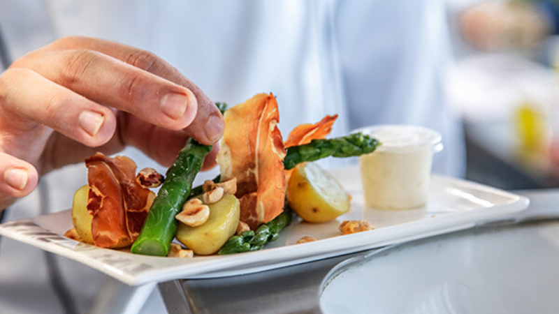Hand plating asparagus, potatoes and crisp vegetables on a fine dining dish.
