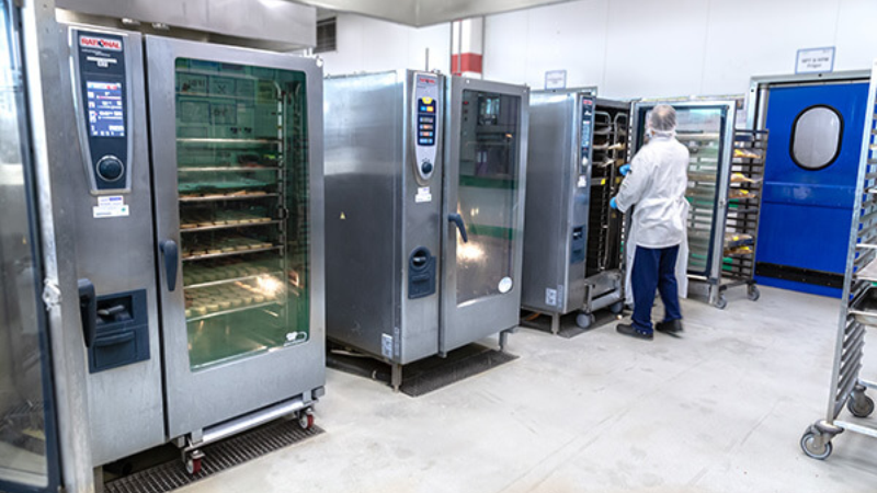 Worker beside RATIONAL SelfCooking Center combi ovens in a professional kitchen.