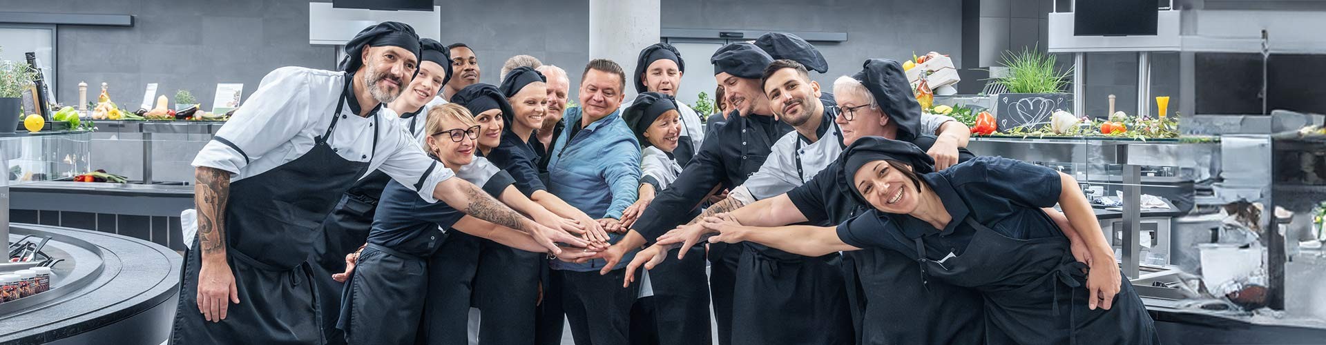 Küchenteam steht mit zusammengelegten Händen in Profiküche.
