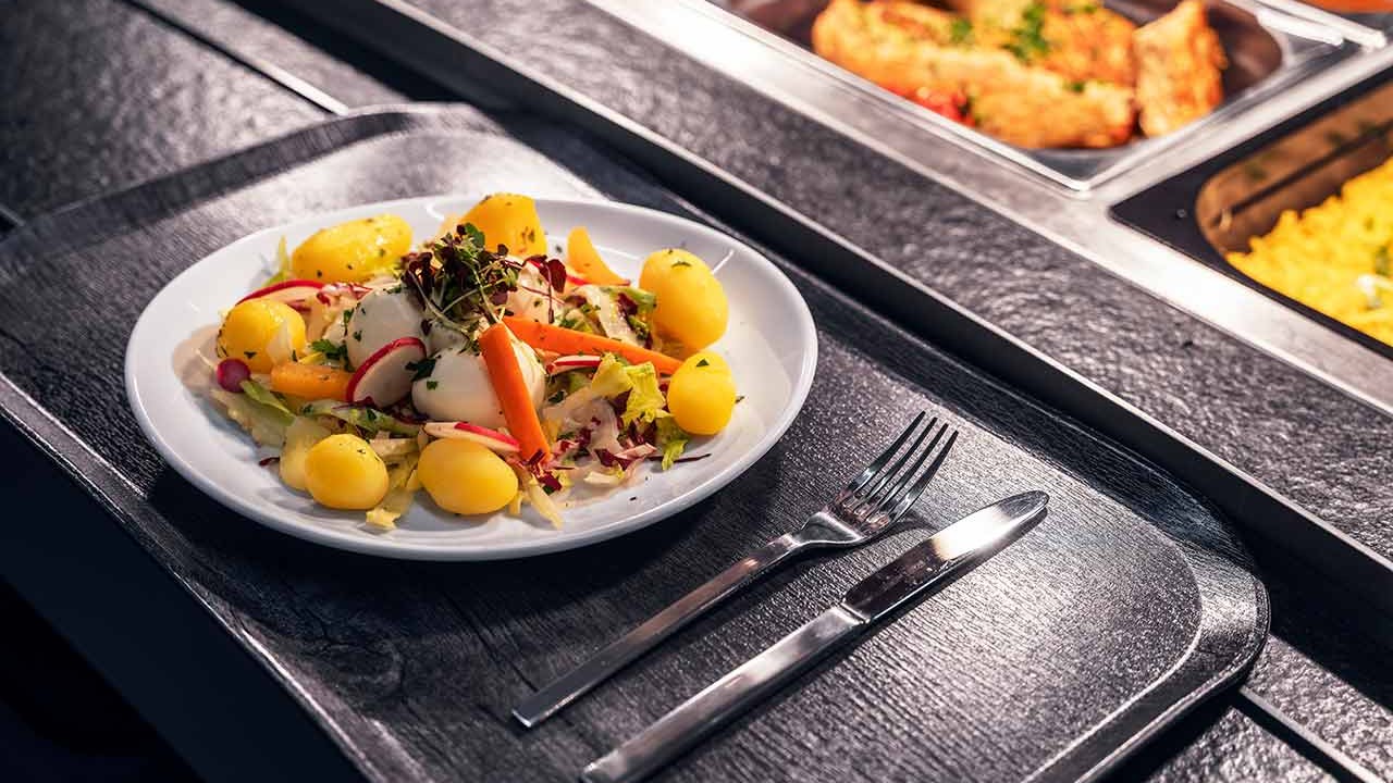 Teller mit Salat, Mozzarella, Drillingen und Gemüse auf Buffettheke.