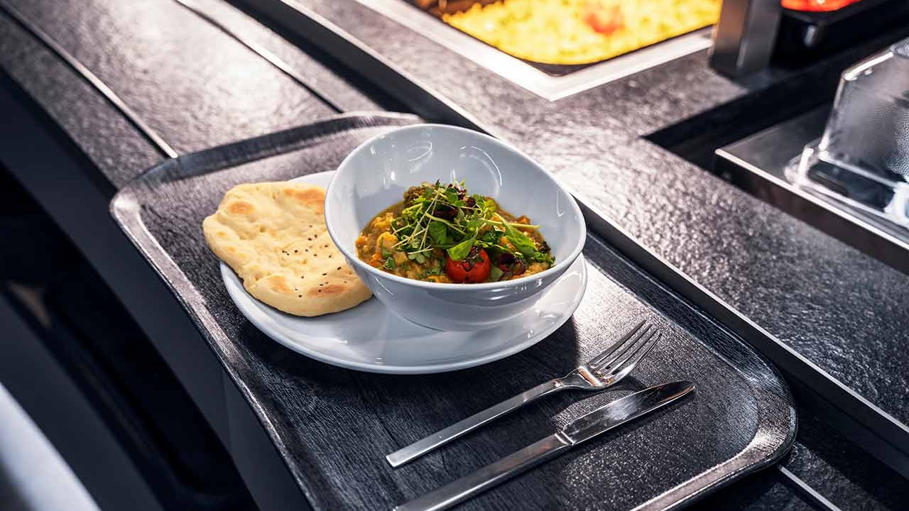 Schale mit Gemüsecurry, Kräutern und Fladenbrot auf Buffettheke.