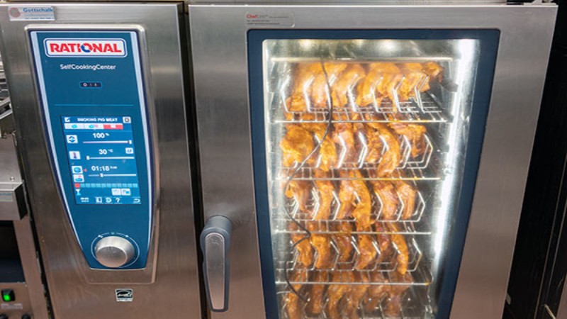 A Rational SelfCookingCenter oven with multiple racks of roasting ribs visible through its glass door.