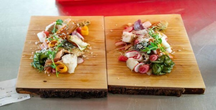Zwei angerichtete Gourmetgerichte auf rustikalen Holzbrettern.