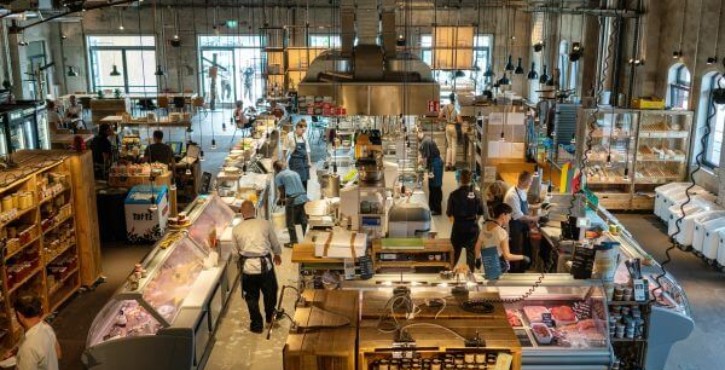 Weitblick in die HOBENKÖÖK Markthalle mit offener Küche und Gästen.