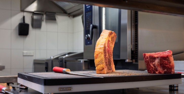 Rohe Fleischstücke auf Schneidebrett vor RATIONAL iHexagon Kombidämpfer.