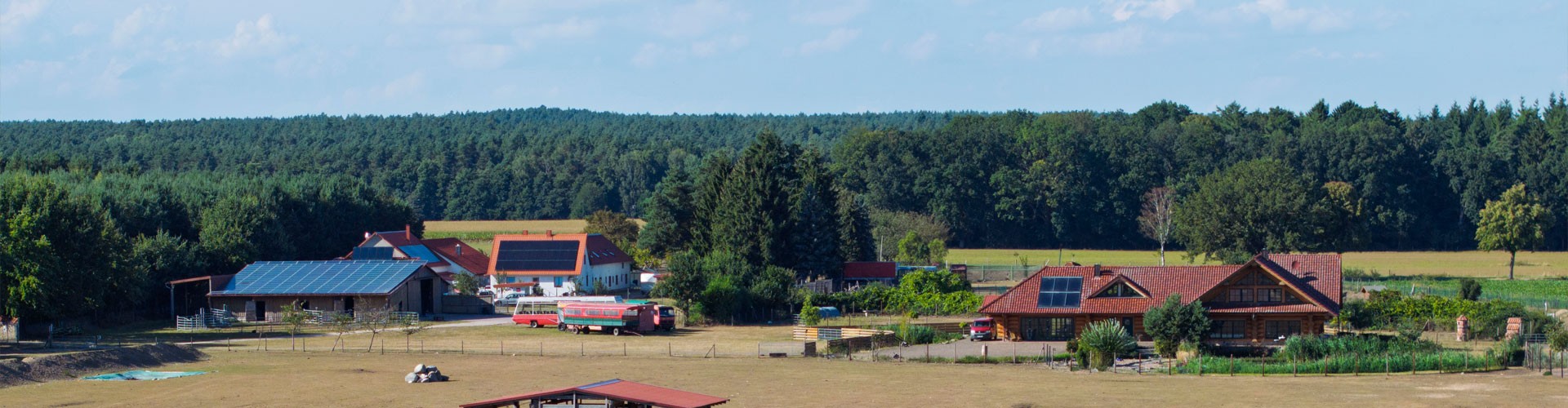Panoramic view of rural farm buildings with solar panels surrounded by forest and fields.