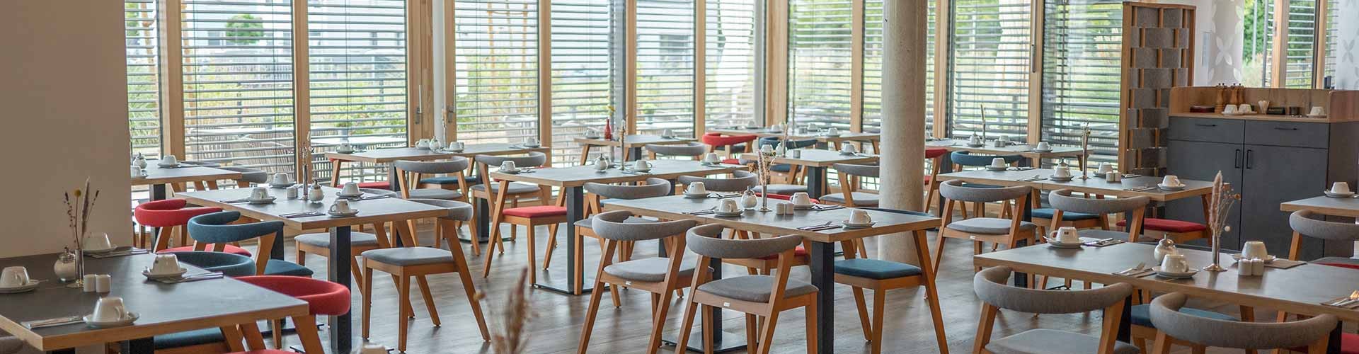 Heller Restaurantbereich mit gedeckten Tischen und großen Fenstern.
