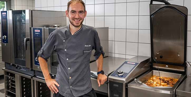 Lächelnder Koch neben RATIONAL iCombi Pro und iVario in einer Profiküche.