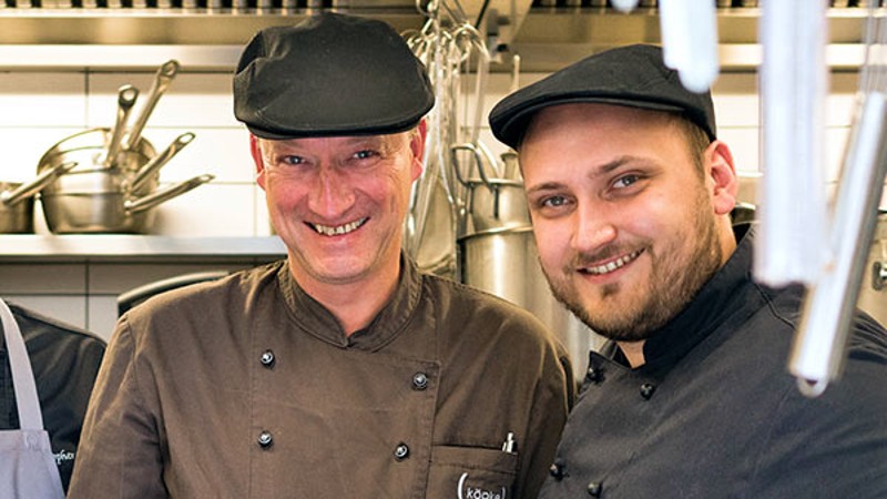 Zwei lächelnde Köche in einer professionellen Küche.