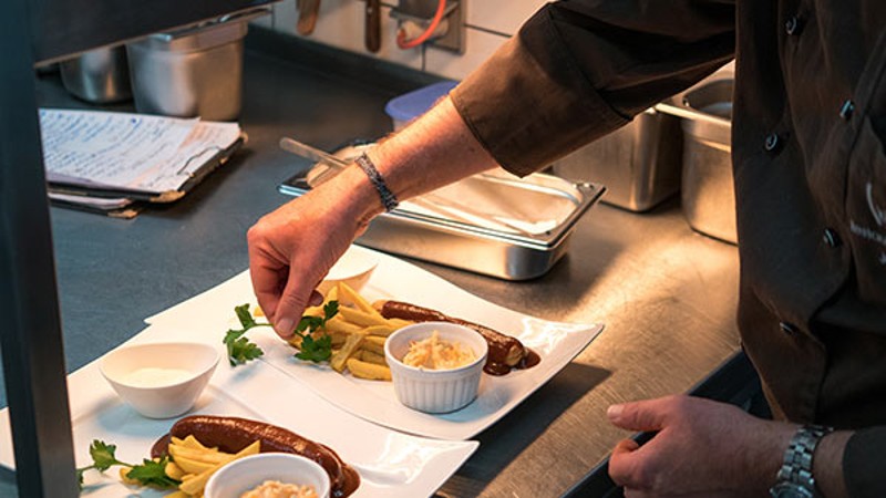 Koch garniert angerichtete Würste mit Pommes in einer professionellen Küche.