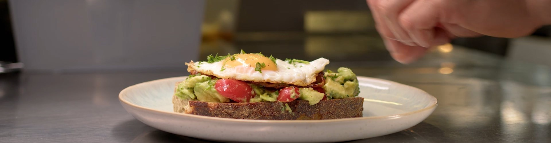 Avocado-Toast mit Spiegelei wird in einer professionellen Küche garniert.