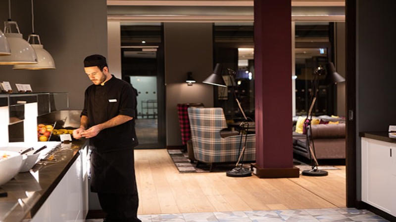 Koch bereitet Speisen an einem Buffetcounter in modernem Restaurantinterieur zu.