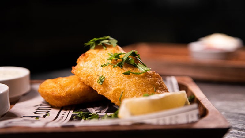 Panierte Fischfilets mit Zitronenspalte auf einem Holztablett serviert.