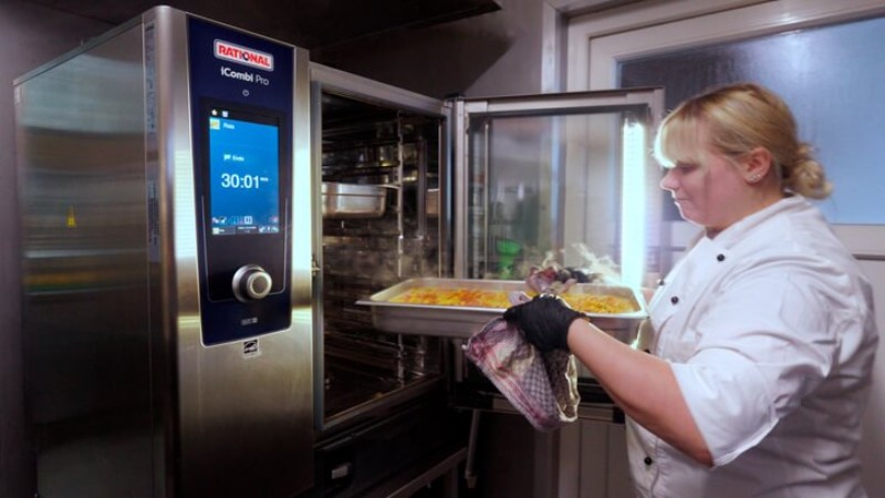 A chef placing a tray of food into a Rational iCombi Pro oven.